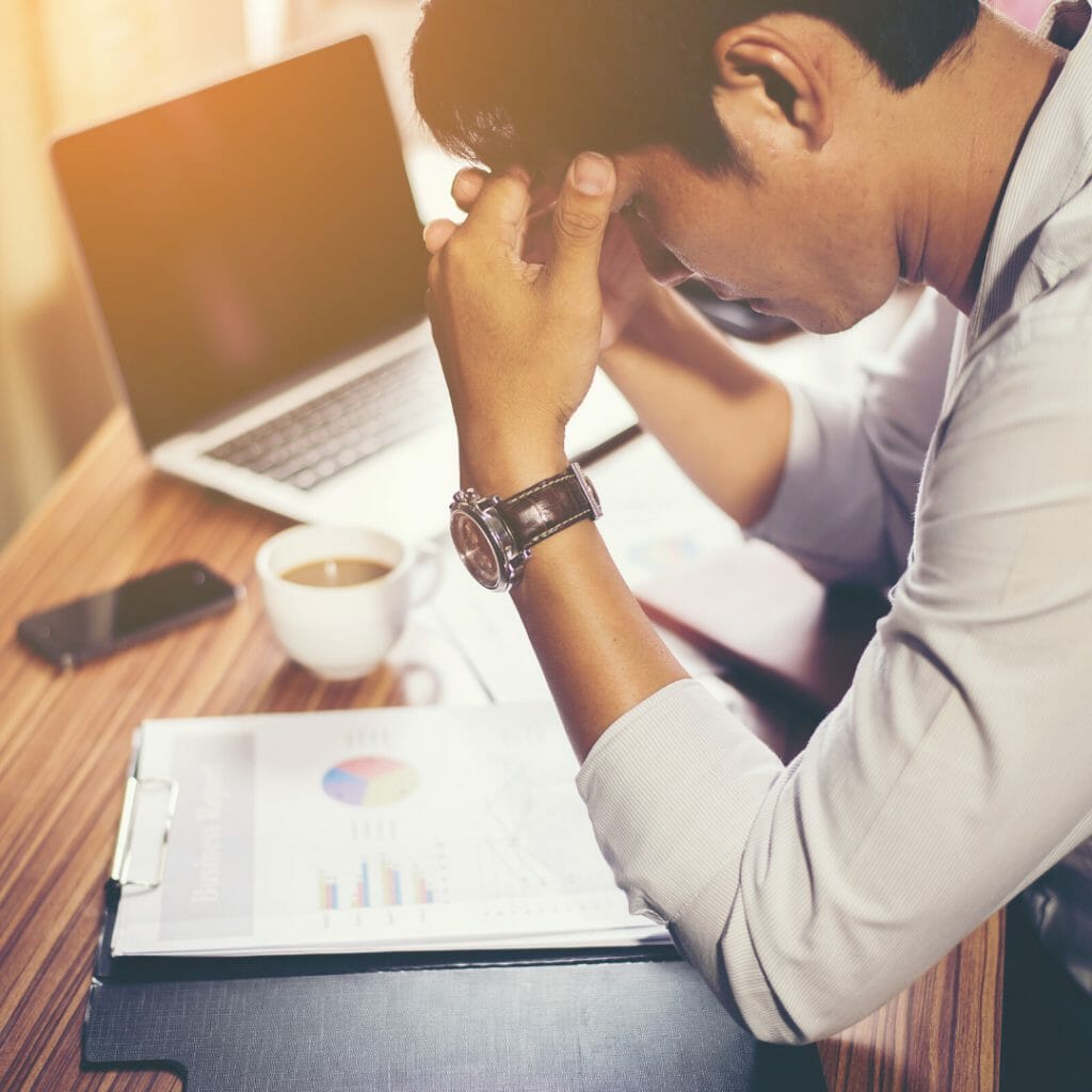 a man with black hair sat with his elbows at his desk worrying about his financial stress